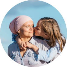 Young girl kisses her mum wearing a pink headscarf on the cheek, both smiling