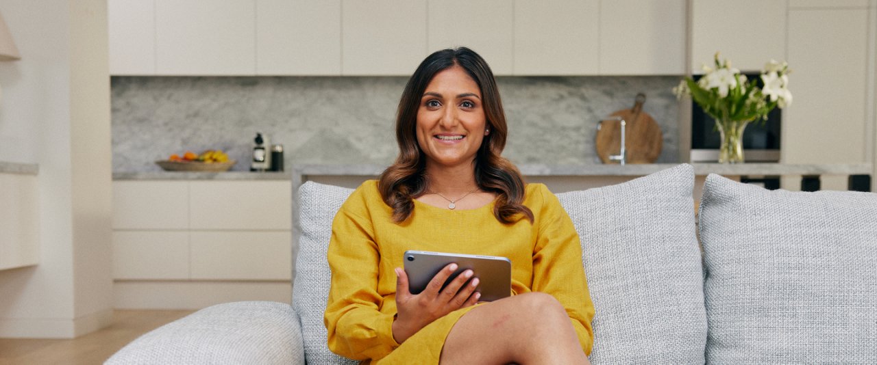A woman sitting on a couch, focused on using a tablet in her hands.