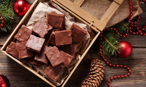 Brownies presented in a box on top of a wooden table with Christmas decorations.