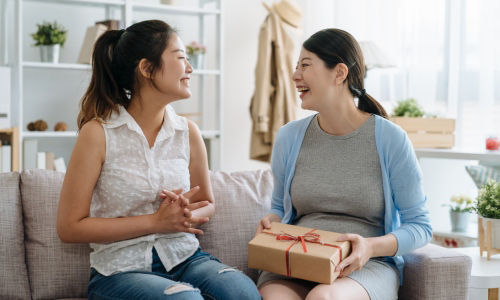 Young smiling female friends sitting on a couch, with one holding a gift