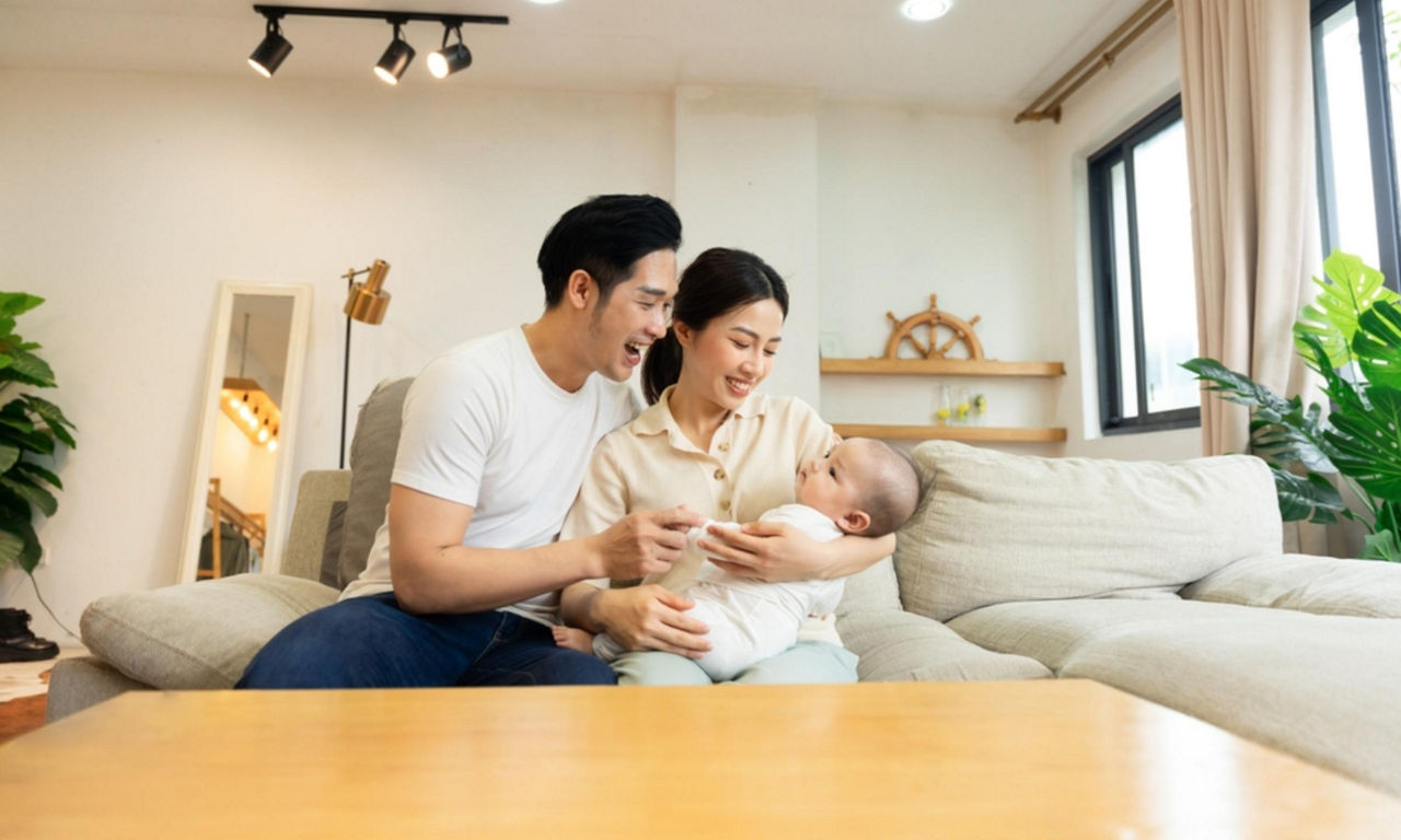 A father and mother smiling at their baby while they are in the living room 