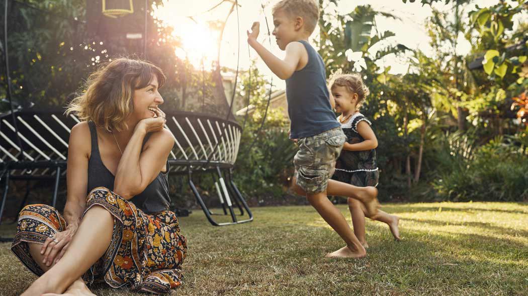 a woman is sitting and 2 kids are playing in a garden