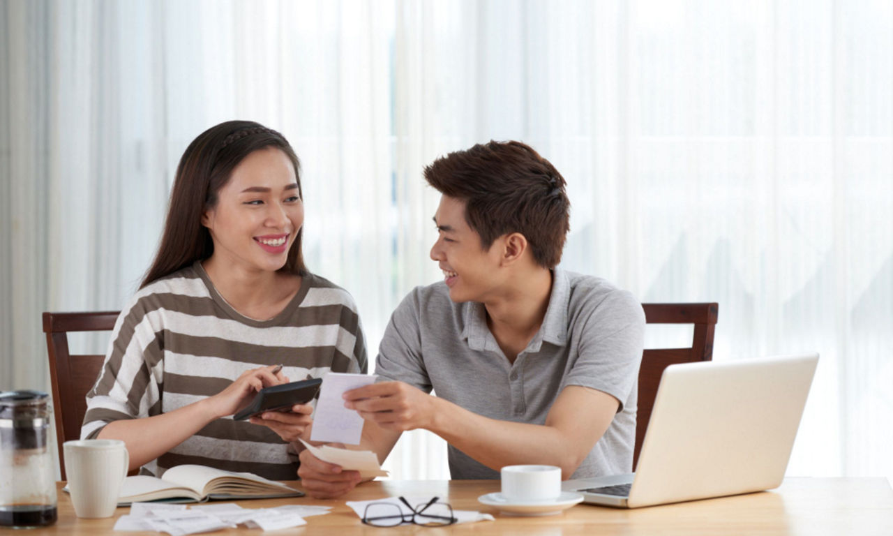 Young couple holding receipts and a calculator discuss family budget at the dining table