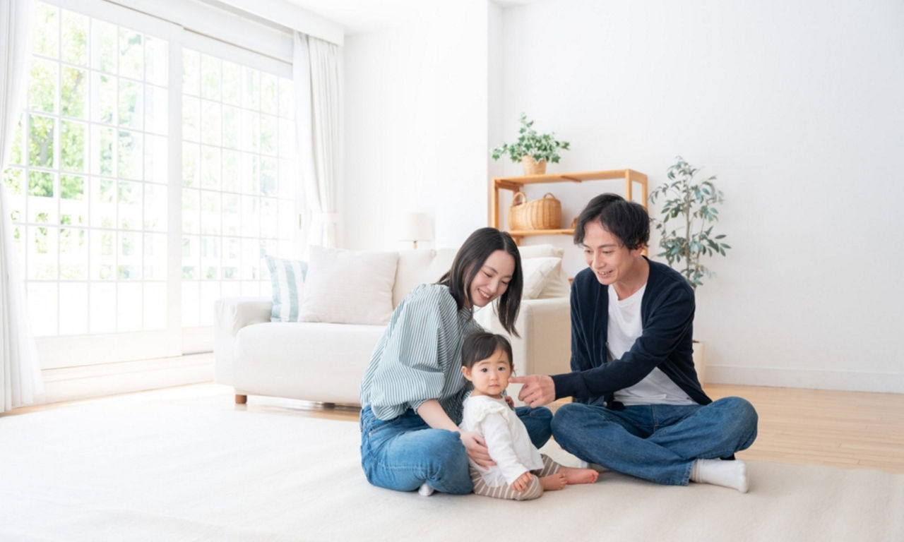 Asian couple with a baby sitting on the living room floor beside the sofa