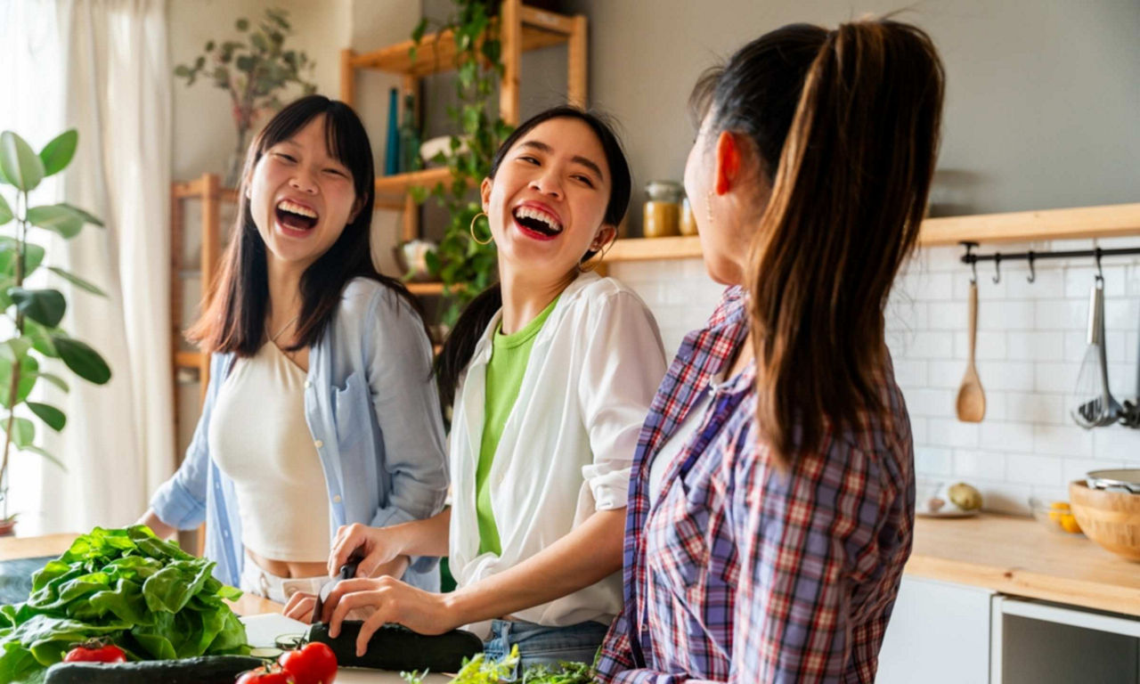 Asian friends laughing while cooking together in the kitchen  