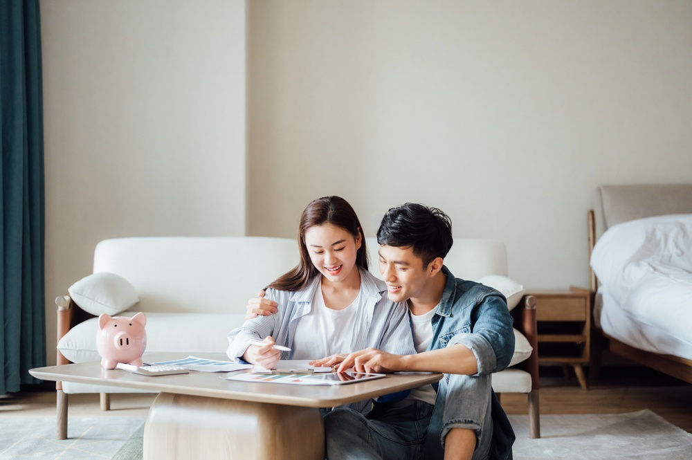 Couple discussing on the bedroom floor with papers and piggybank on the table.