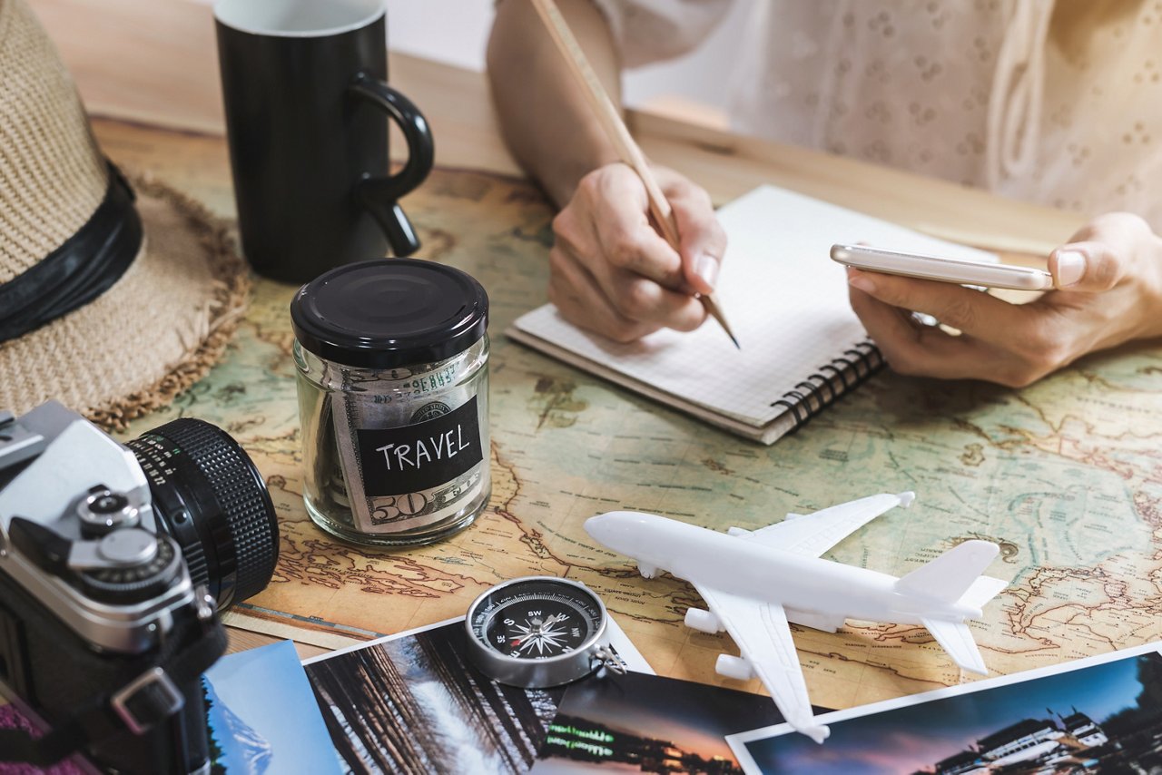 Woman writes on notebook and uses calculator while planning vacation. 