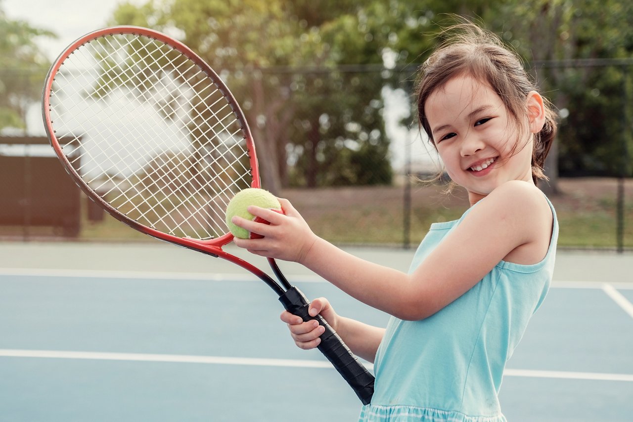 Young Asian girl on a tennis court, holding a tennis racket and tennis ball