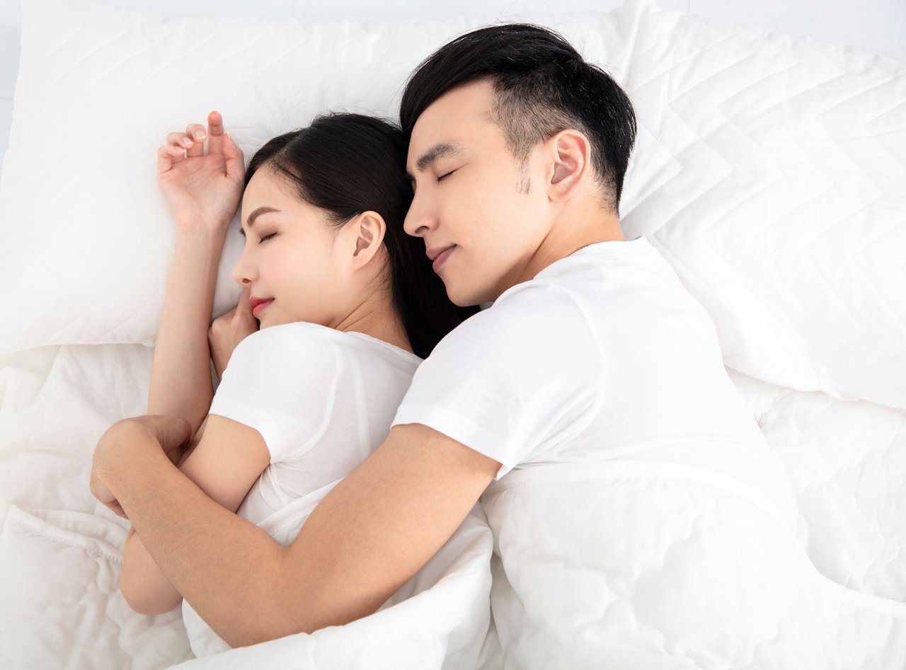 Asian couple lying in bed asleep thanks to good sleep hygiene 