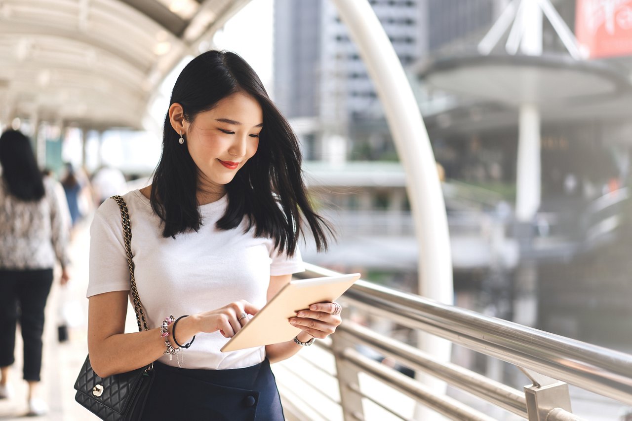 A smiling girl looking at her digital tablet while walking on the street 