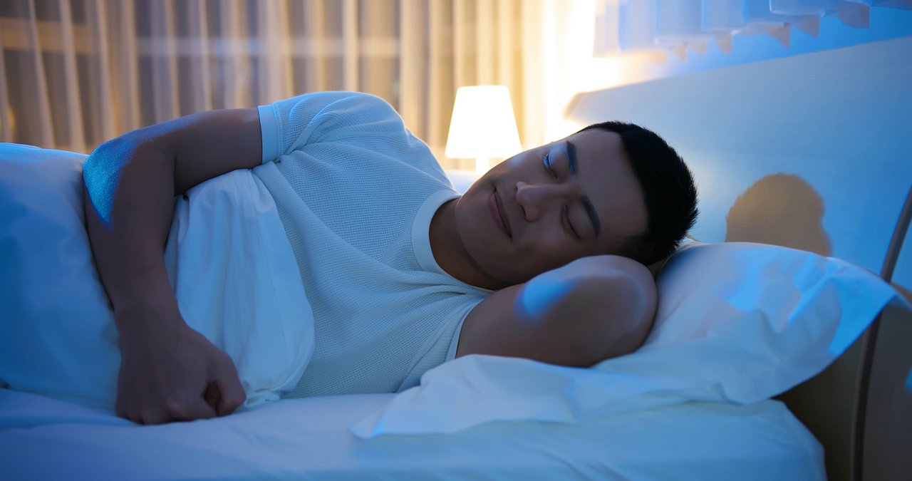 Asian man lying in bed and sleeping with a smile at night