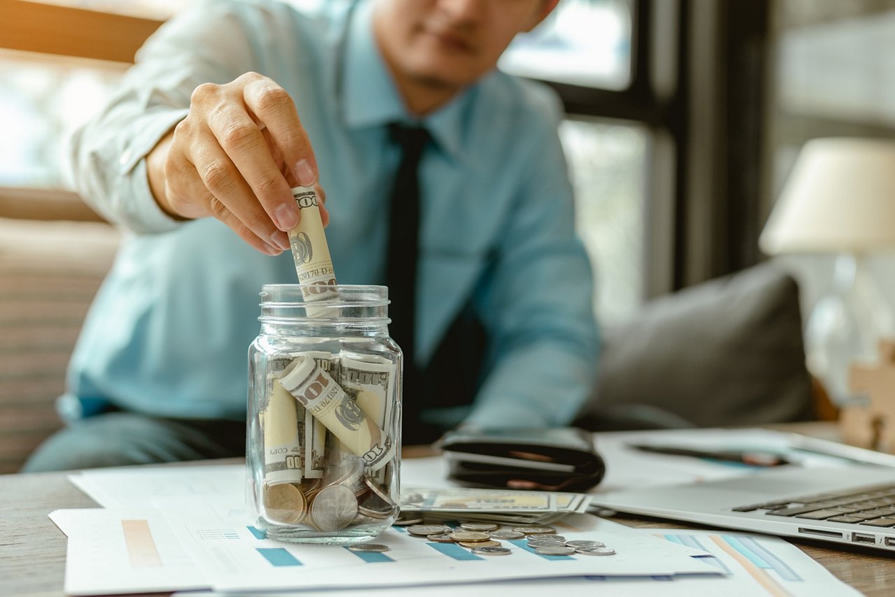 Businessman puts money in a glass jar. 
