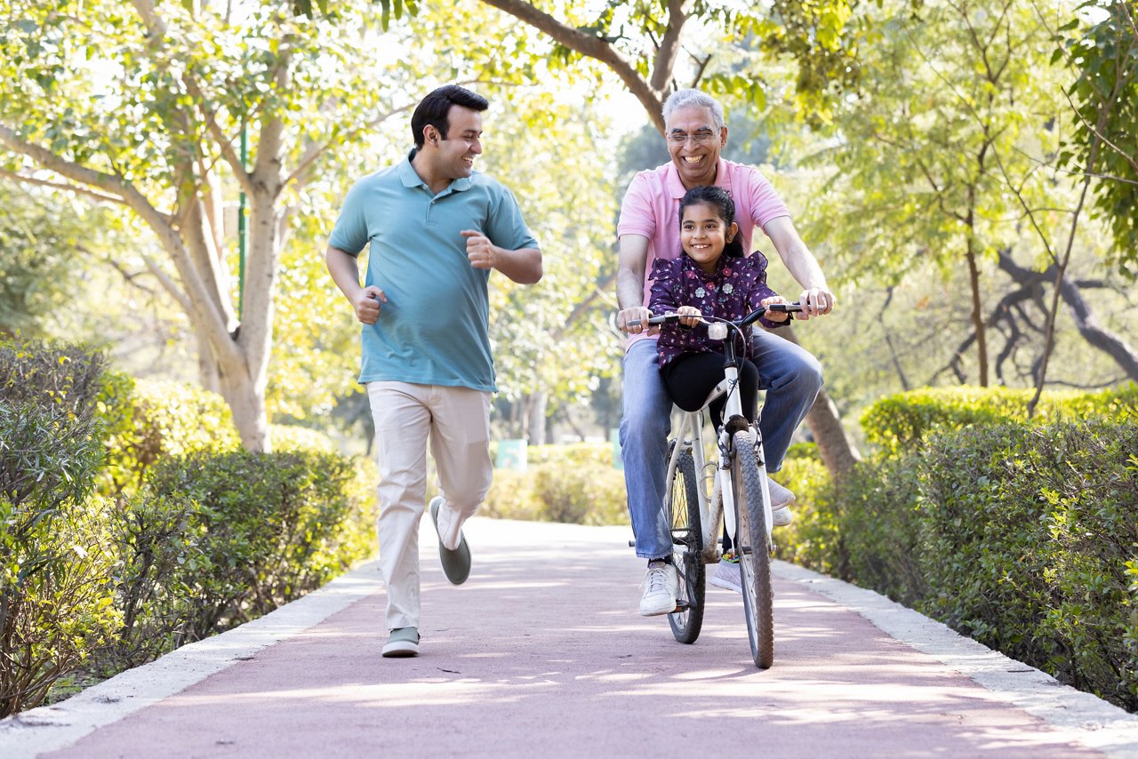 A man jogging next to a senior man riding bicycle with a girl