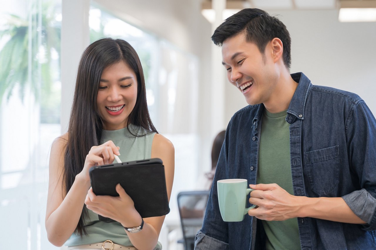 A smiling woman looking at her male colleague's phone