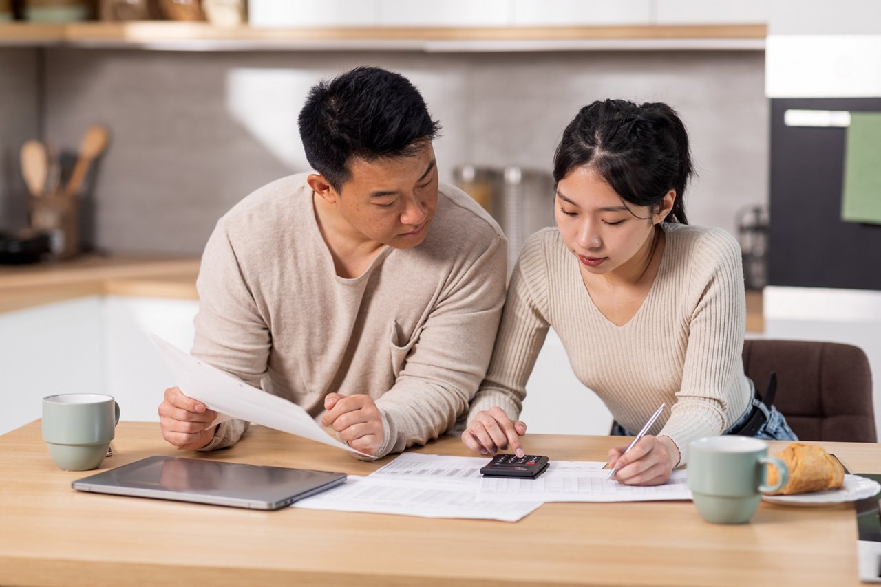 Asian couple go through documents and use calculator while in the kitchen