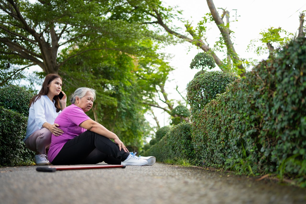 Young woman on the phone as an elderly lady in pain sits on the ground 
