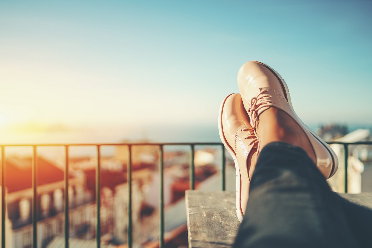 Feet with shoes on top of a table with blurred background of a city near the sea