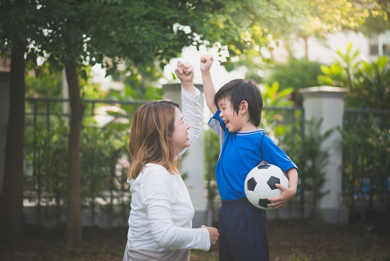 Asian mom and her son holding a soccer ball, cheering after sports activities