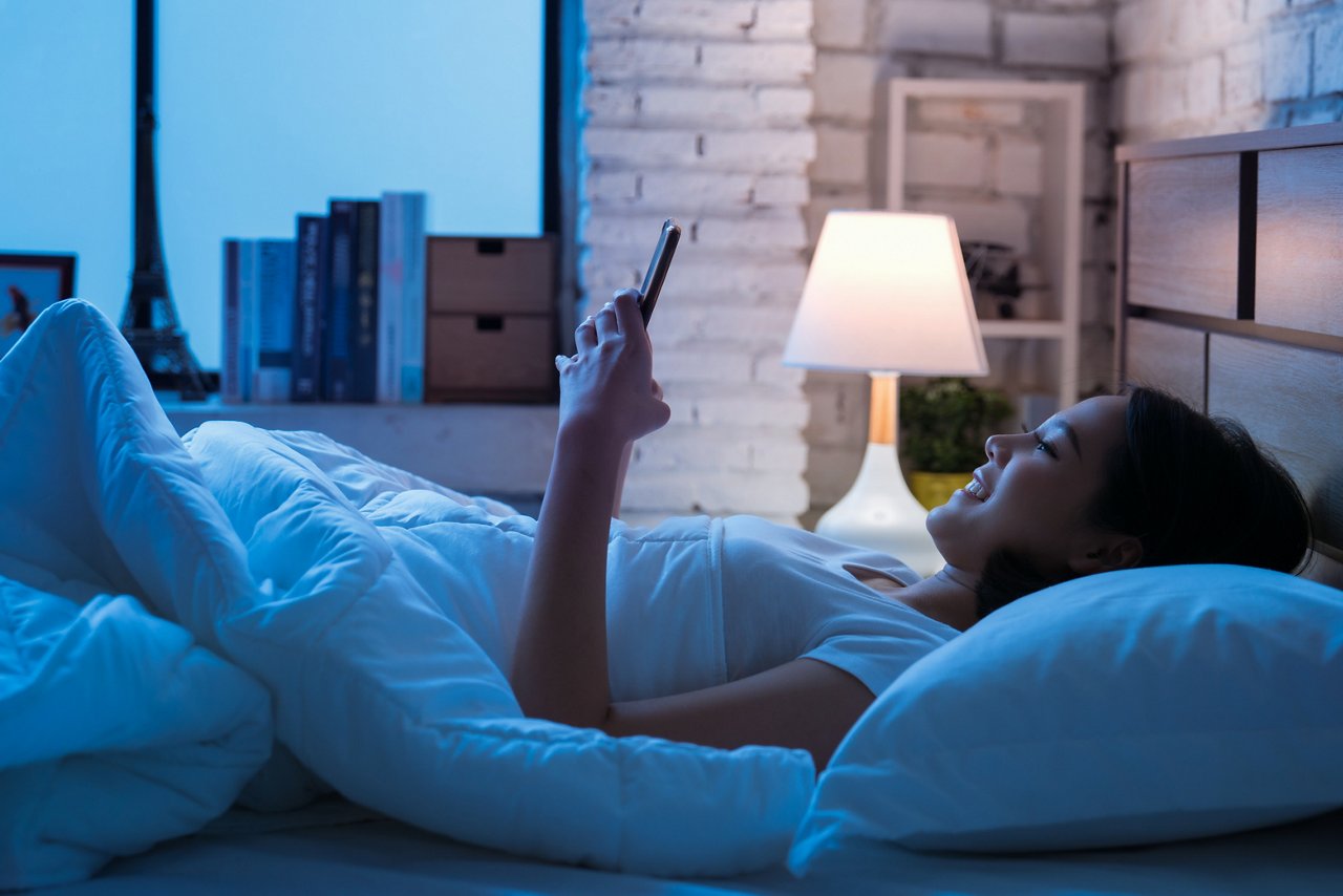 一位亞洲女性躺在床上玩手機