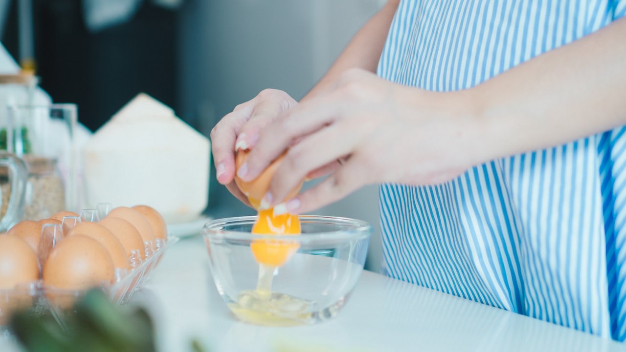 Pregnant woman cracks an egg into a bowl  