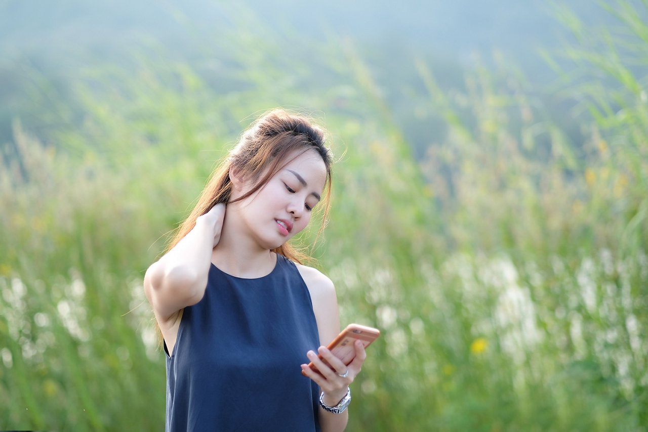 Woman holds her neck, staring at her mobile phone