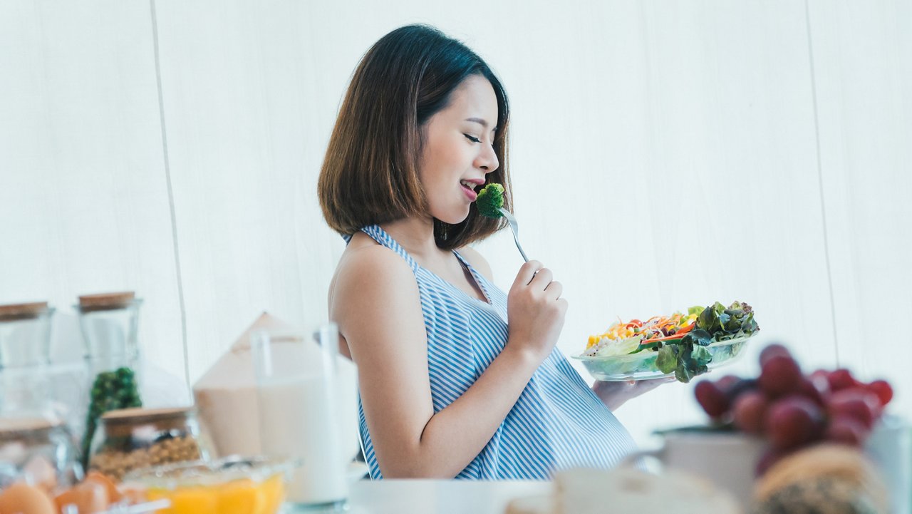 Pregnant woman eating vegetable salad happily 