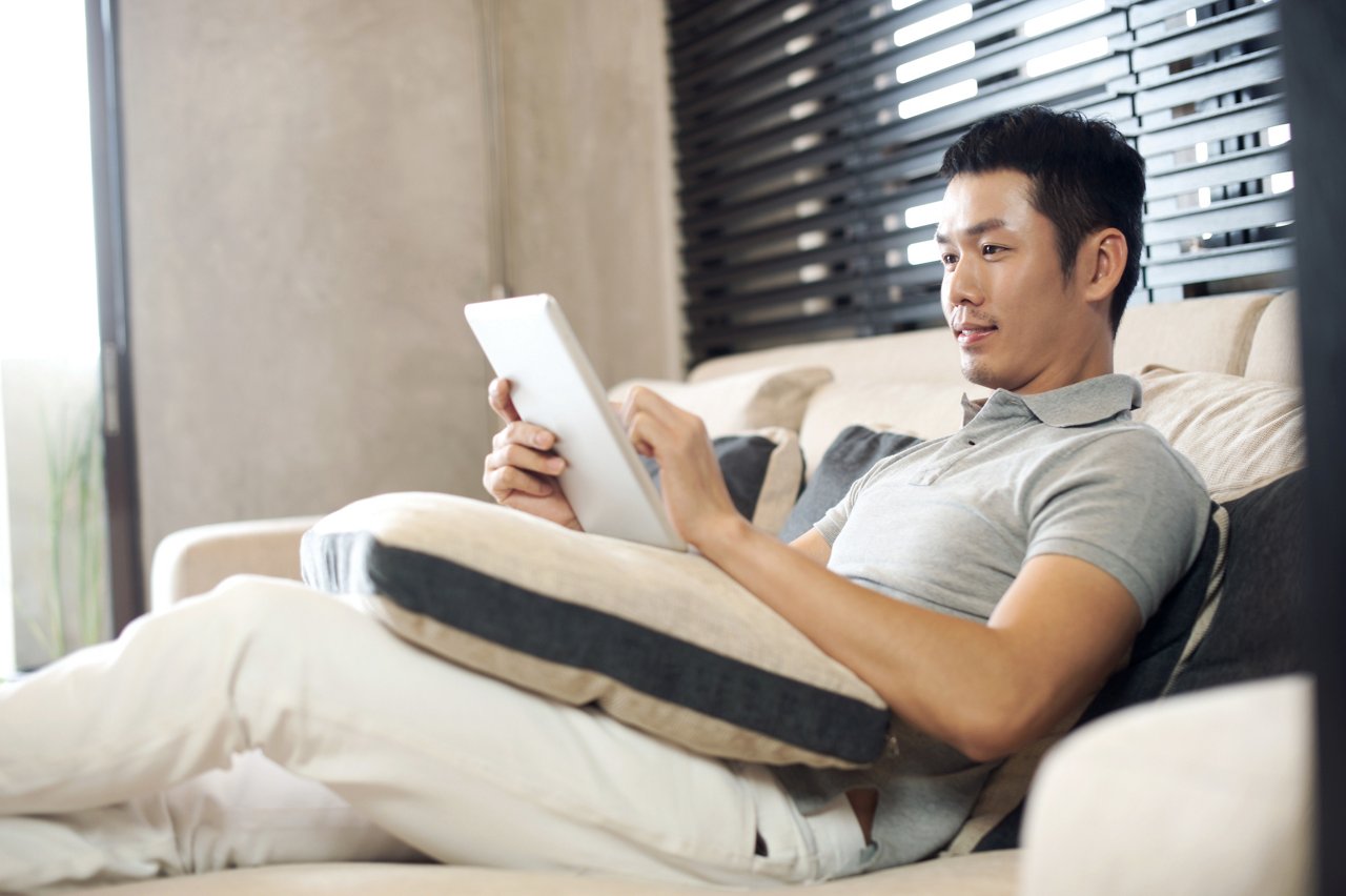 A man working on his digital tablet while lounging on a sofa 