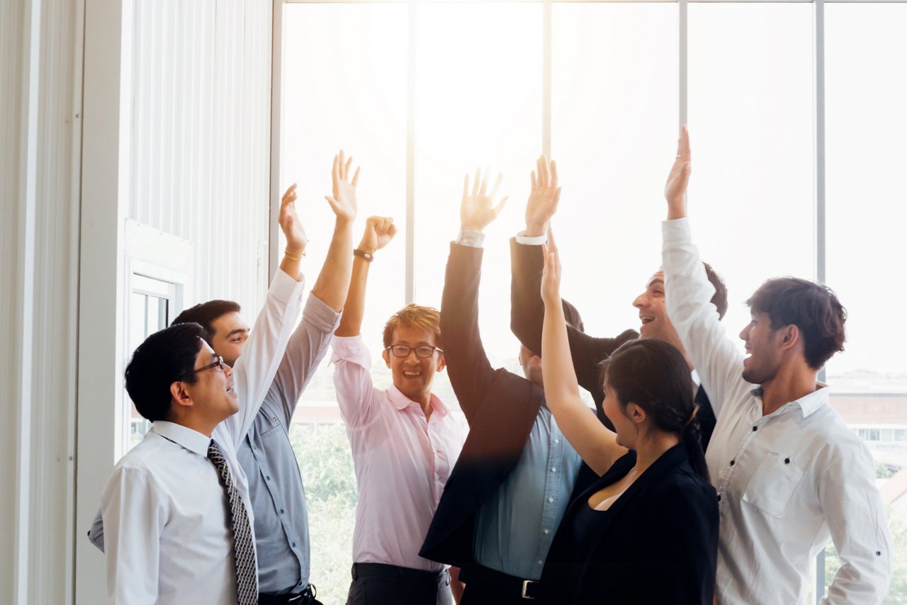 Group of multiethnic business men and woman raising hands up giving high five in sunny office