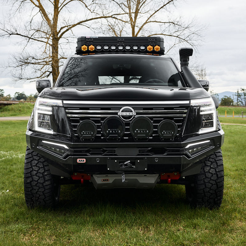Front view of a Nissan Patrol Y63 fitted with an ARB bull bar, driving lights, roof rack, snorkel and under-vehicle protection, parked on grass.
