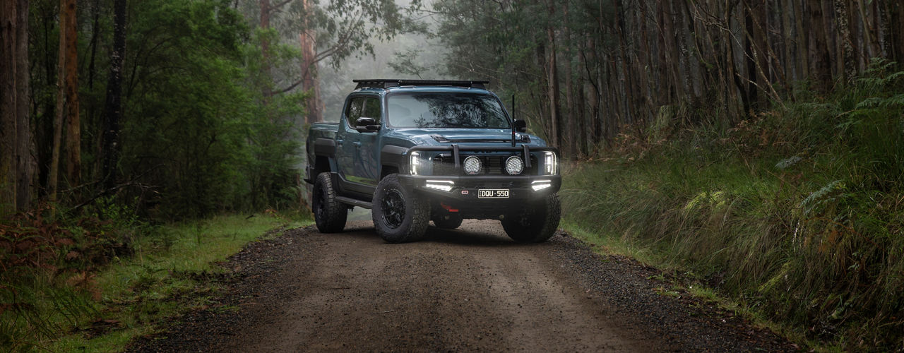 Kia Tasman in a road in the woods.