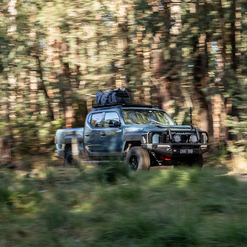 Kia Tasman in a road in the woods.