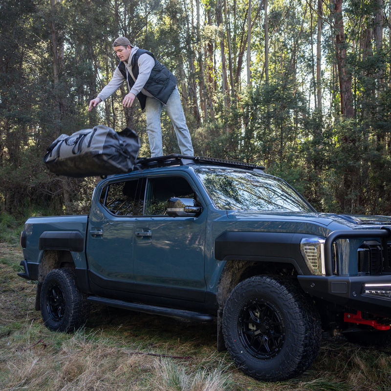 Young mand unloading the back of a blue Kia Tasman.