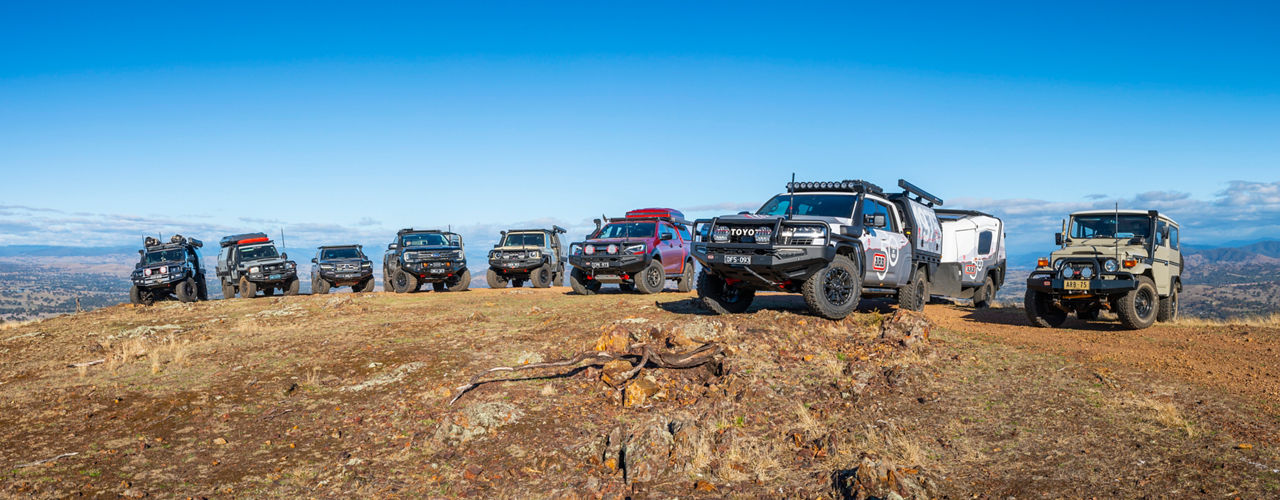 Line-up of ARB equipped 4WD vehicles and an ARB Earth Camper parked on a rocky ridgeline overlooking a mountain landscape.
