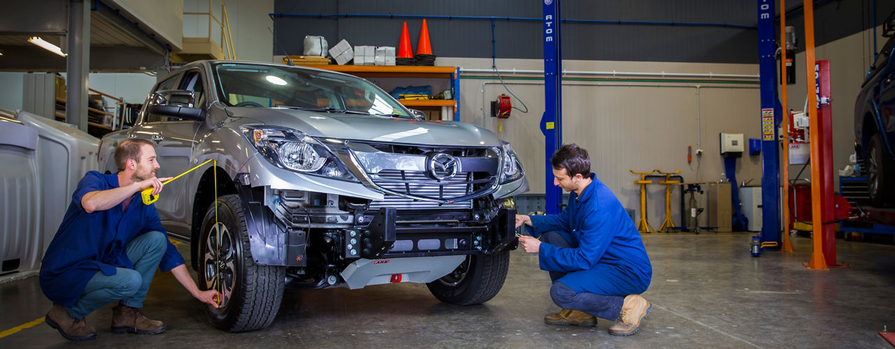 Wide view of an ARB workshop with two technicians fitting a bull bar to a Mazda BT-50.