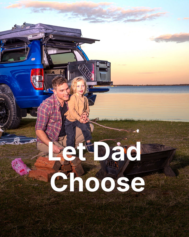 Father and child toasting marshmallows by a campfire next to an ARB-equipped blue Ford Ranger at sunset.