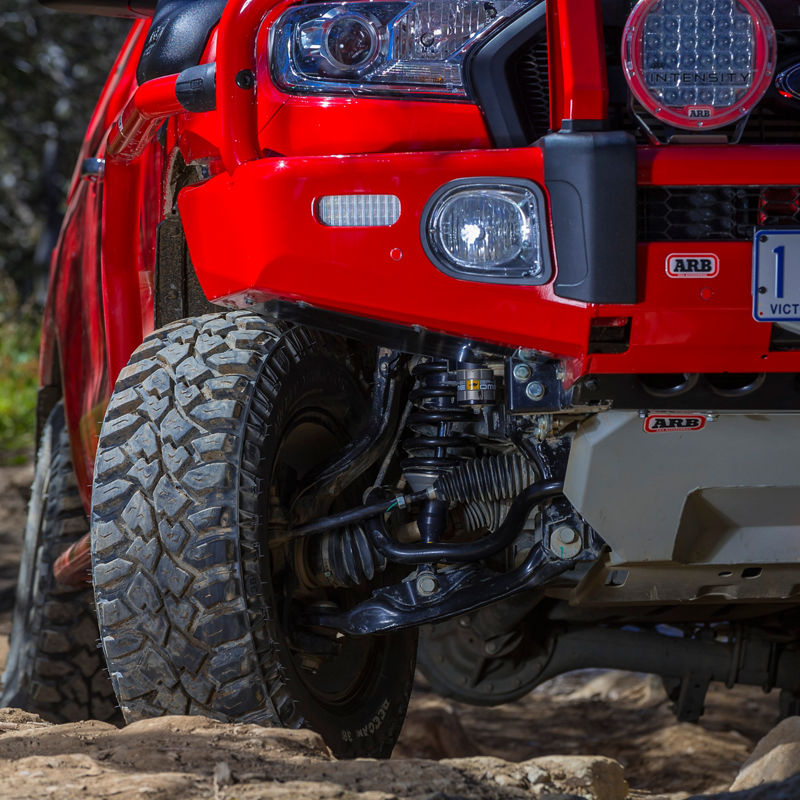 Close-up view of a Ford Ranger PXII front end showing an ARB bull bar, driving lights, under-vehicle protection and front suspension articulation on rocky terrain.