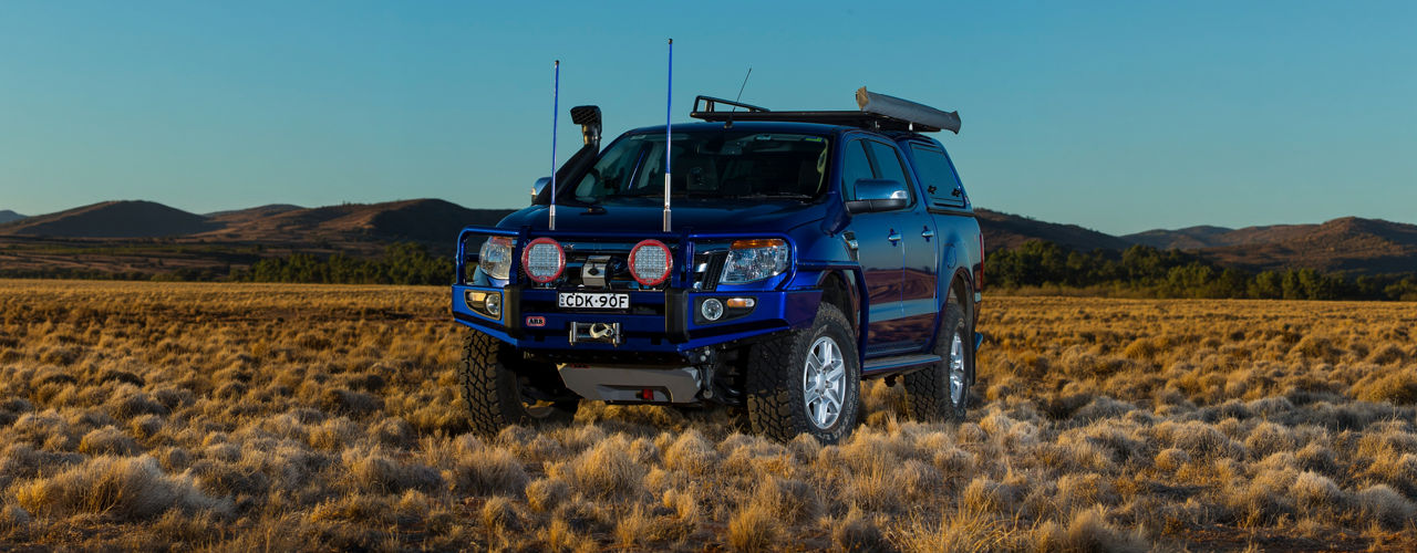 Ford Ranger PX fitted with an ARB bull bar, driving lights, snorkel, canopy and awning, parked in a dry grassland landscape with rolling hills in the background.