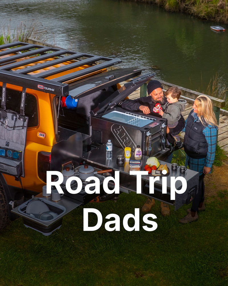 Family accessing ARB drawer system and fridge slide on an orange 4WD parked beside a river.
