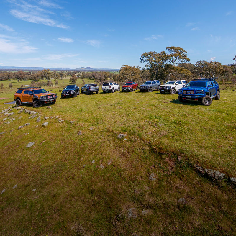 Group of Ford Ranger vehicles parked on a grassy ridgeline overlooking a rural landscape beneath a clear blue sky.