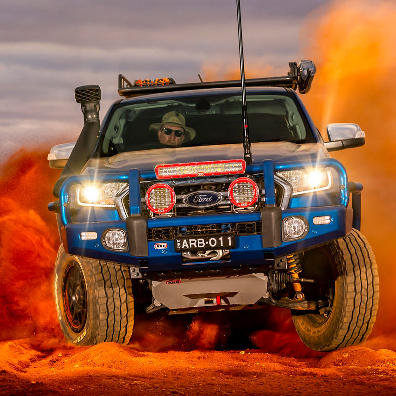 Front view of a Ford Ranger PXIII fitted with an ARB bull bar, driving lights, LED light bar, snorkel, roof rack and under-vehicle protection, driving through red outback sand.