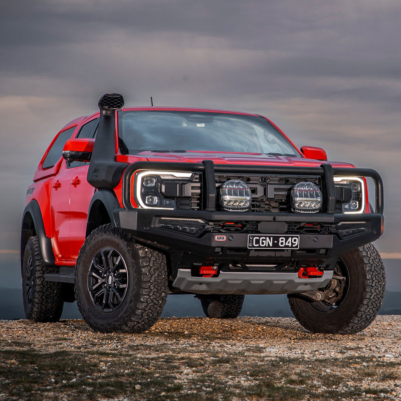 Ford Ranger Raptor fitted with an ARB bull bar, driving lights, snorkel and under vehicle protection, parked on a gravel ridgeline beneath a dramatic overcast sky.