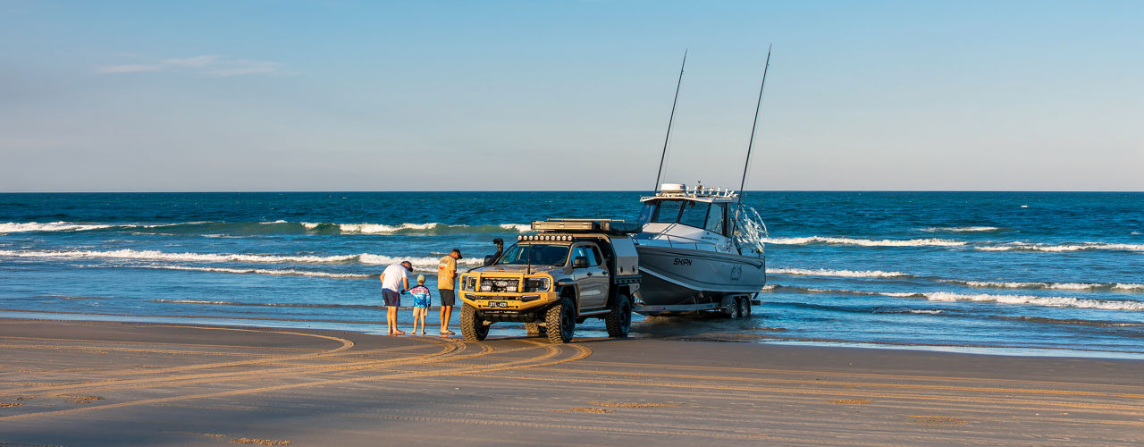 Ford Ranger Super Duty parked on a beach beside a boat trailer, while three people stand near the shoreline.