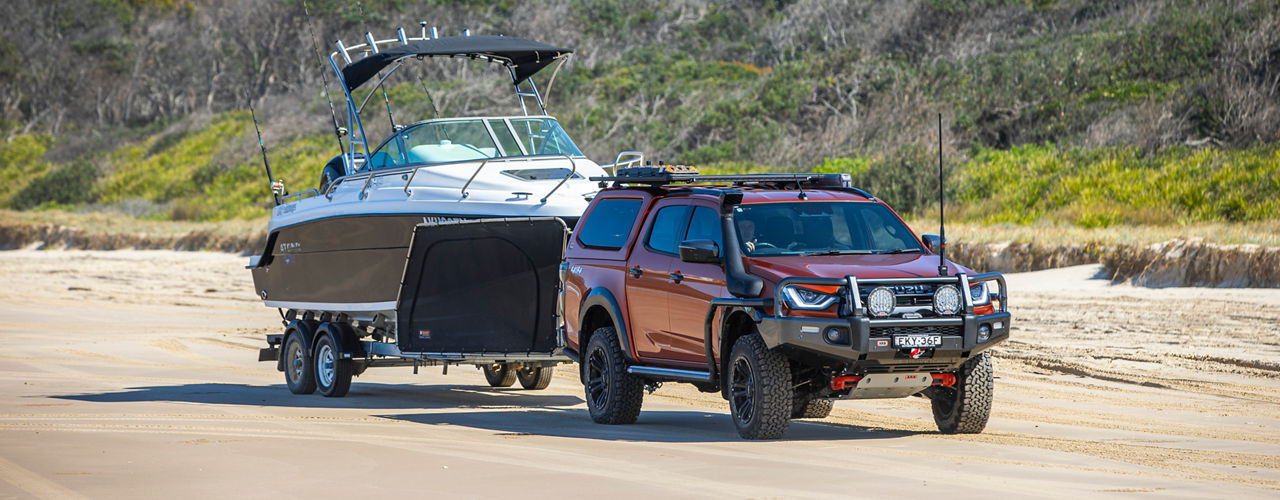 Isuzu D-MAX towing a boat trailer along a sandy beach, fitted with an ARB bull bar, canopy, roof rack system and snorkel.