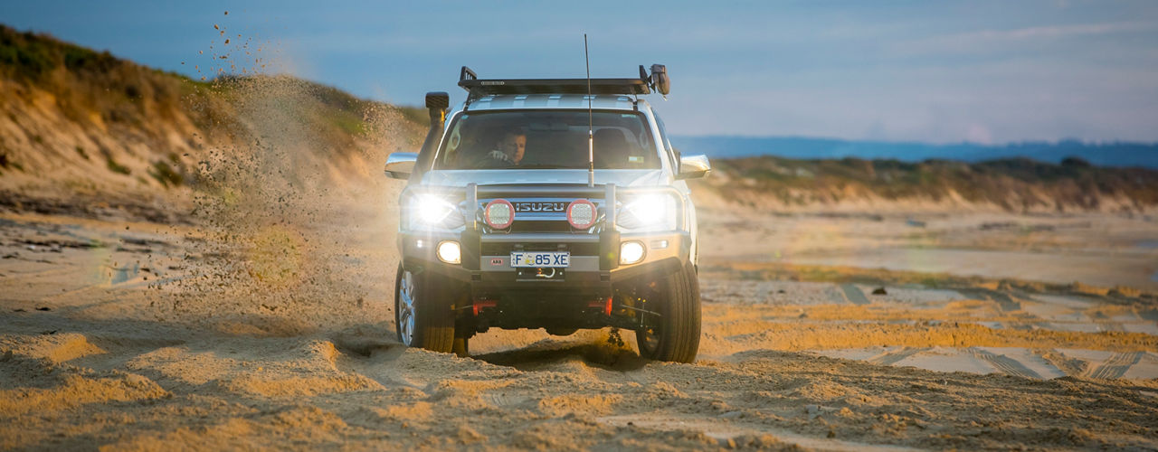 Front view of an ARB equipped Isuzu MU-X driving through sand on a coastal beach track.