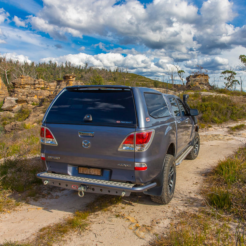 Rear three quarter view of an ARB equipped Mazda BT-50 with a canopy and rear protection on a rocky off road track.