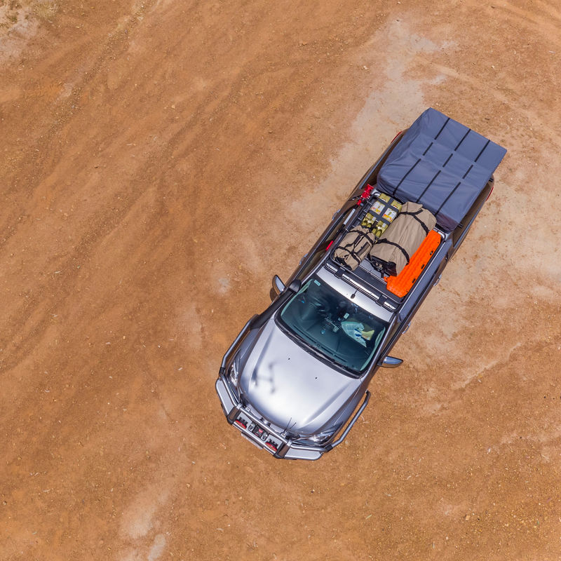 Aerial view of an ARB equipped Mazda BT-50 fitted with a roof rack system and touring gear, parked on a dirt surface.