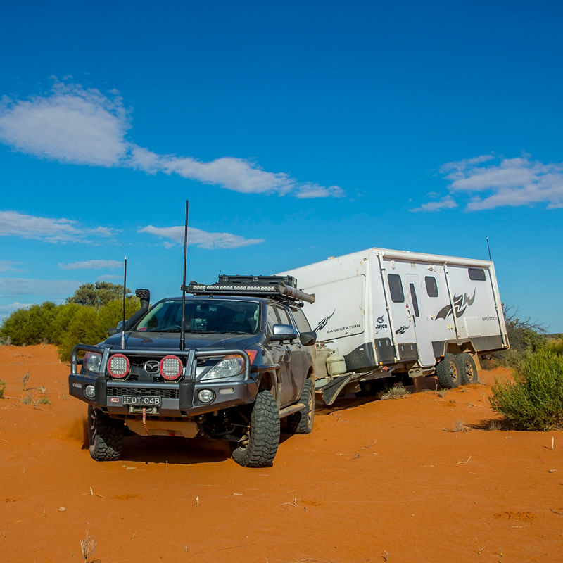 ARB equipped Mazda BT-50 towing an off road camper trailer through a red sand desert landscape.