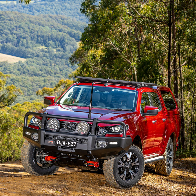 ARB equipped Mazda BT-50 fitted with a bull bar, driving lights, canopy and roof rack system on a forested off road track.