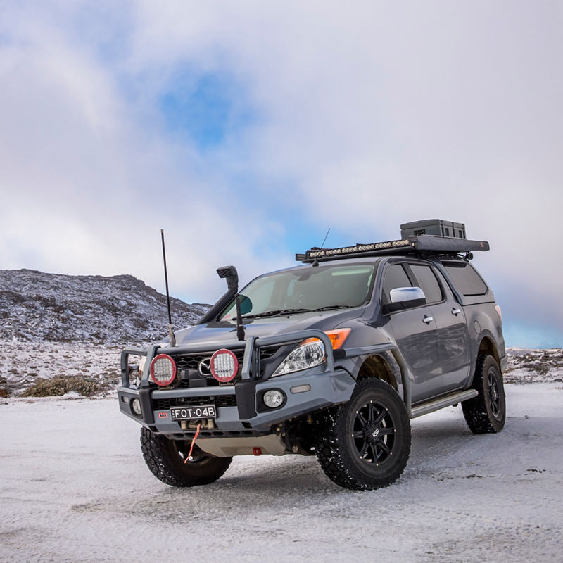 ARB equipped Mazda BT-50 parked on a snow covered mountain landscape with a bull bar, driving lights, canopy and roof rack system.