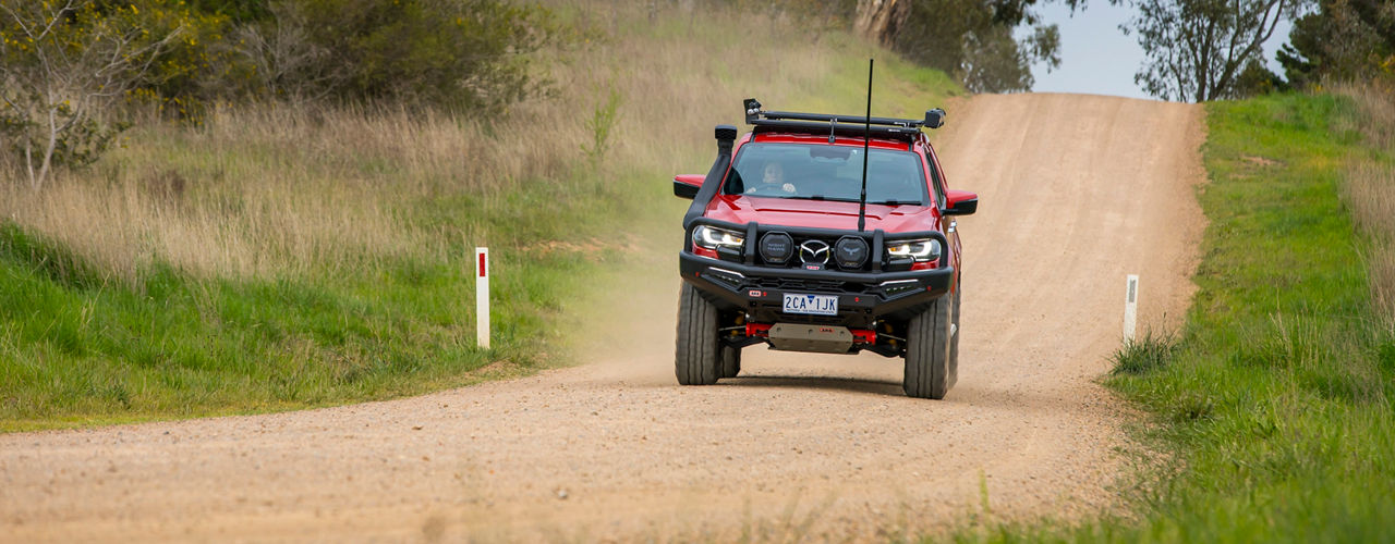 Front view of an ARB equipped Mazda BT-50 driving along a gravel country road with dust trailing behind the vehicle.